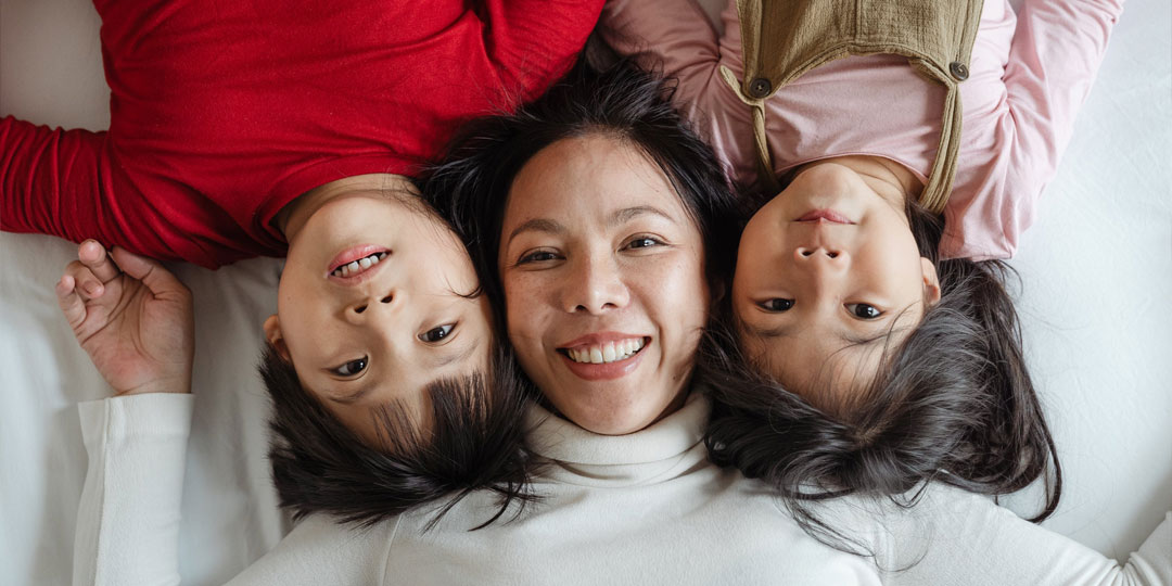 Two children with their mom lying between them smiling on a bed